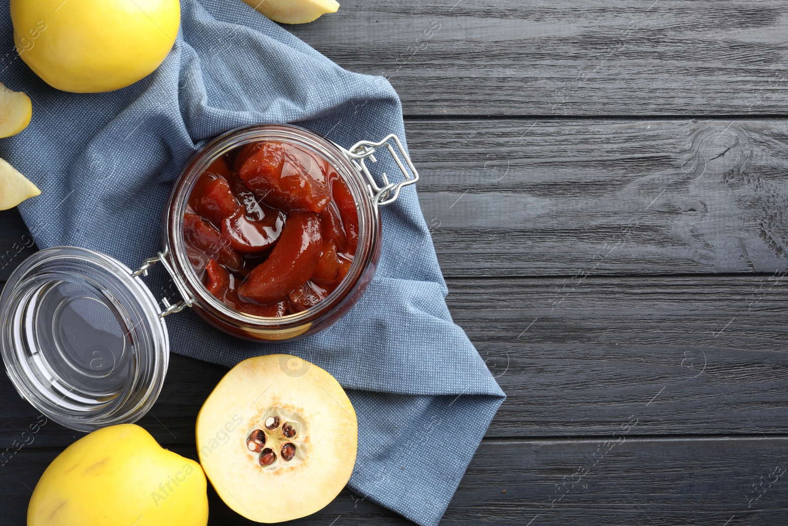 Photo of Quince jam in glass jar and fresh raw fruits on grey wooden table, flat lay. Space for text