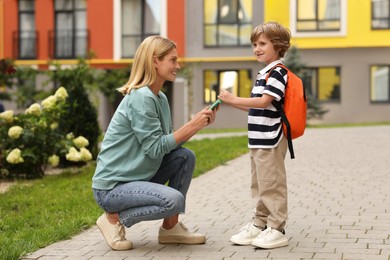 Photo of Happy woman giving notebook to her son near kindergarten outdoors