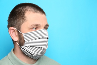 Photo of Man wearing handmade cloth mask on light blue background, space for text. Personal protective equipment during COVID-19 pandemic