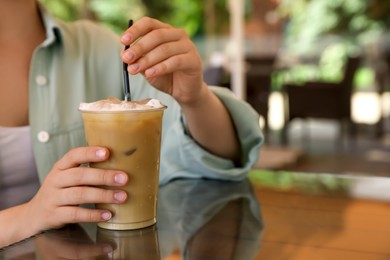Photo of Woman with plastic takeaway cup of delicious iced coffee at table in outdoor cafe, closeup. Space for text