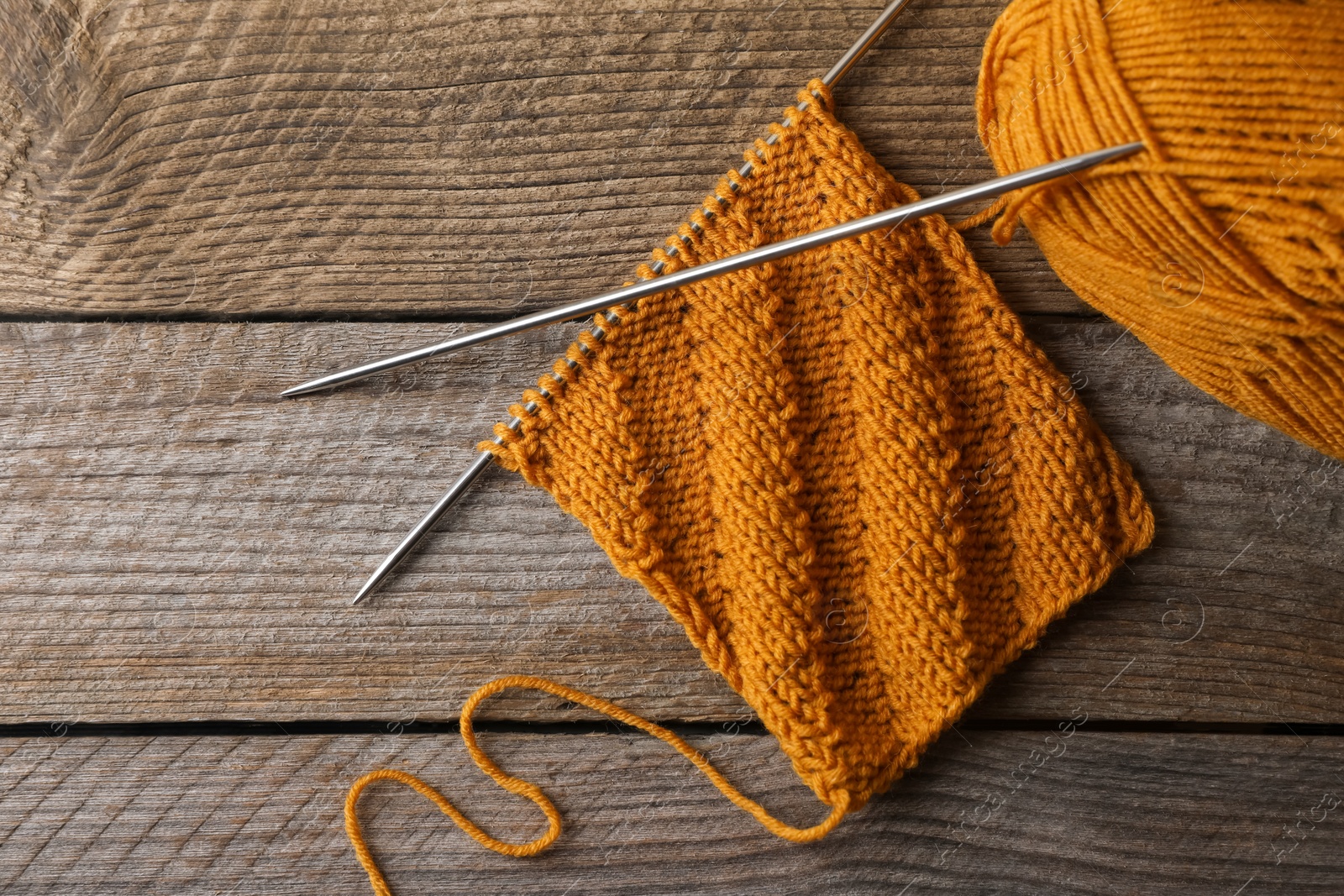 Photo of Soft orange yarn, knitting and metal needles on wooden table, flat lay