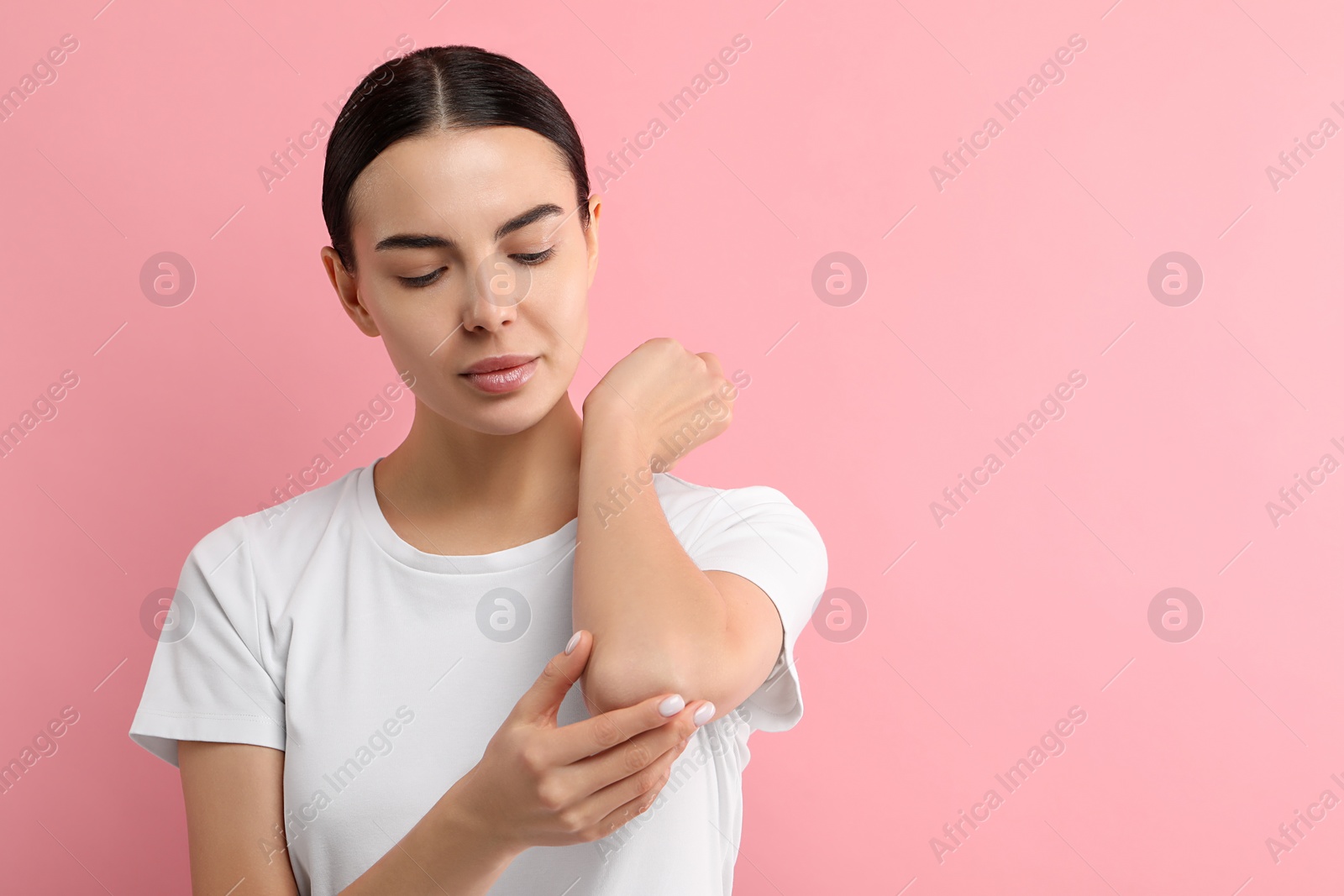 Photo of Woman with dry skin checking her arm on pink background, space for text