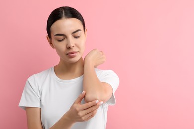 Woman with dry skin checking her arm on pink background, space for text