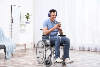 Photo of Happy man with headphones and mobile device in wheelchair at home