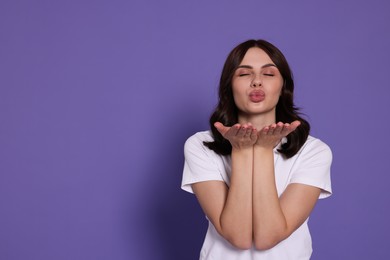 Photo of Beautiful young woman blowing kiss on purple background. Space for text