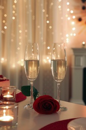 Photo of Romantic table setting with champagne, rose and candles for Valentine's day dinner indoors