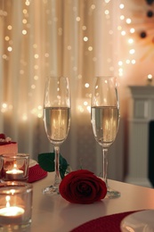 Romantic table setting with champagne, rose and candles for Valentine's day dinner indoors