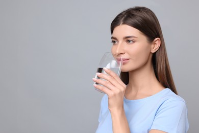 Photo of Healthy habit. Woman drinking fresh water from glass on grey background. Space for text