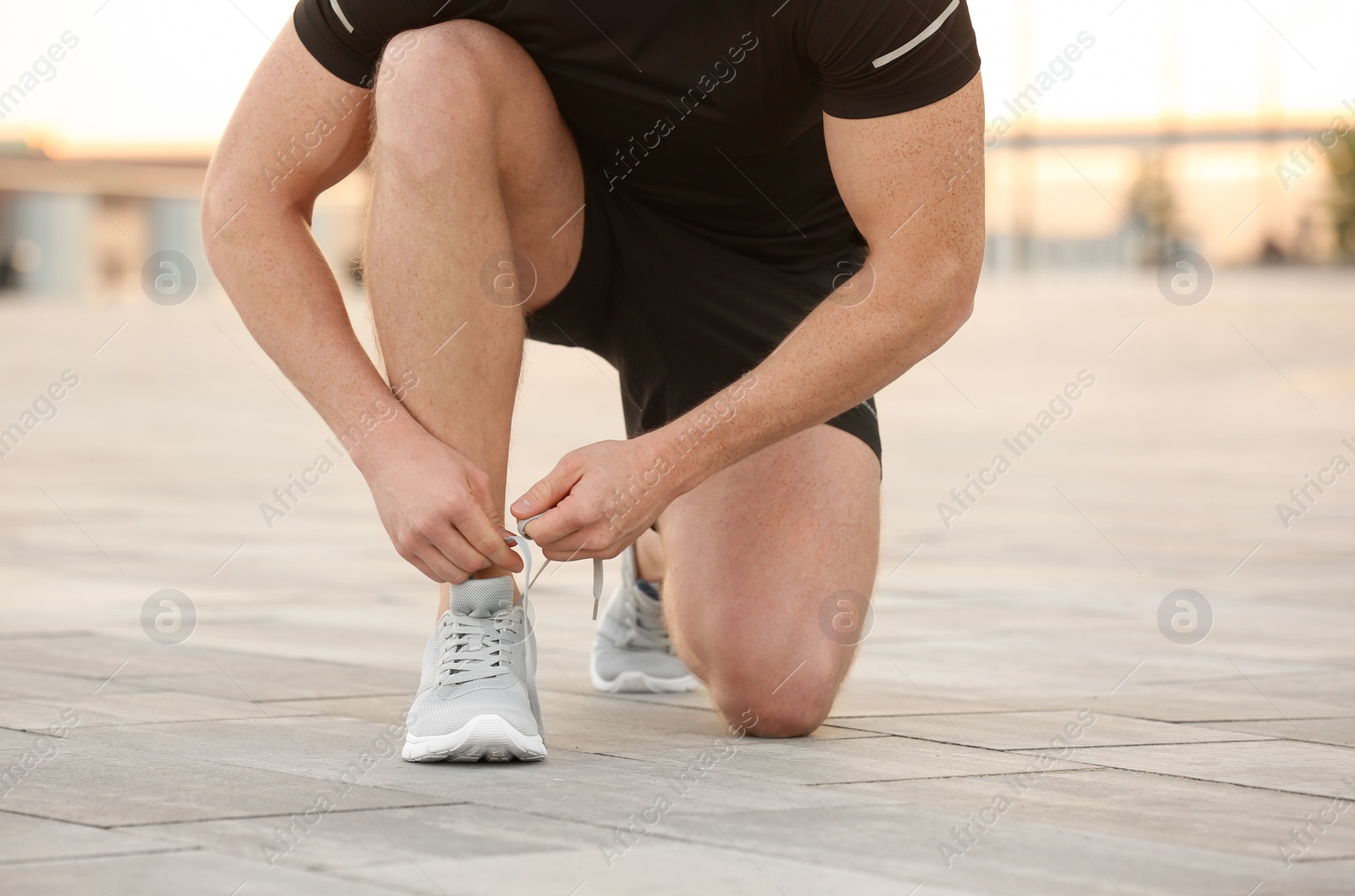 Photo of Young man tying shoelaces before running outdoors, focus on legs