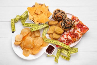 Photo of Different unhealthy food and measuring tape on white wooden table, flat lay. Weight loss concept