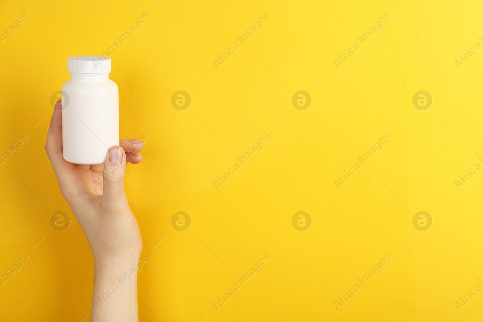 Photo of Woman holding blank white jar of vitamins on yellow background, closeup. Space for text