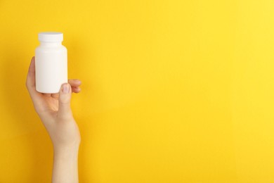 Woman holding blank white jar of vitamins on yellow background, closeup. Space for text