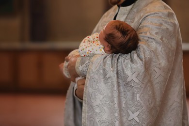 Priest holding adorable baby in church during baptism ceremony, closeup