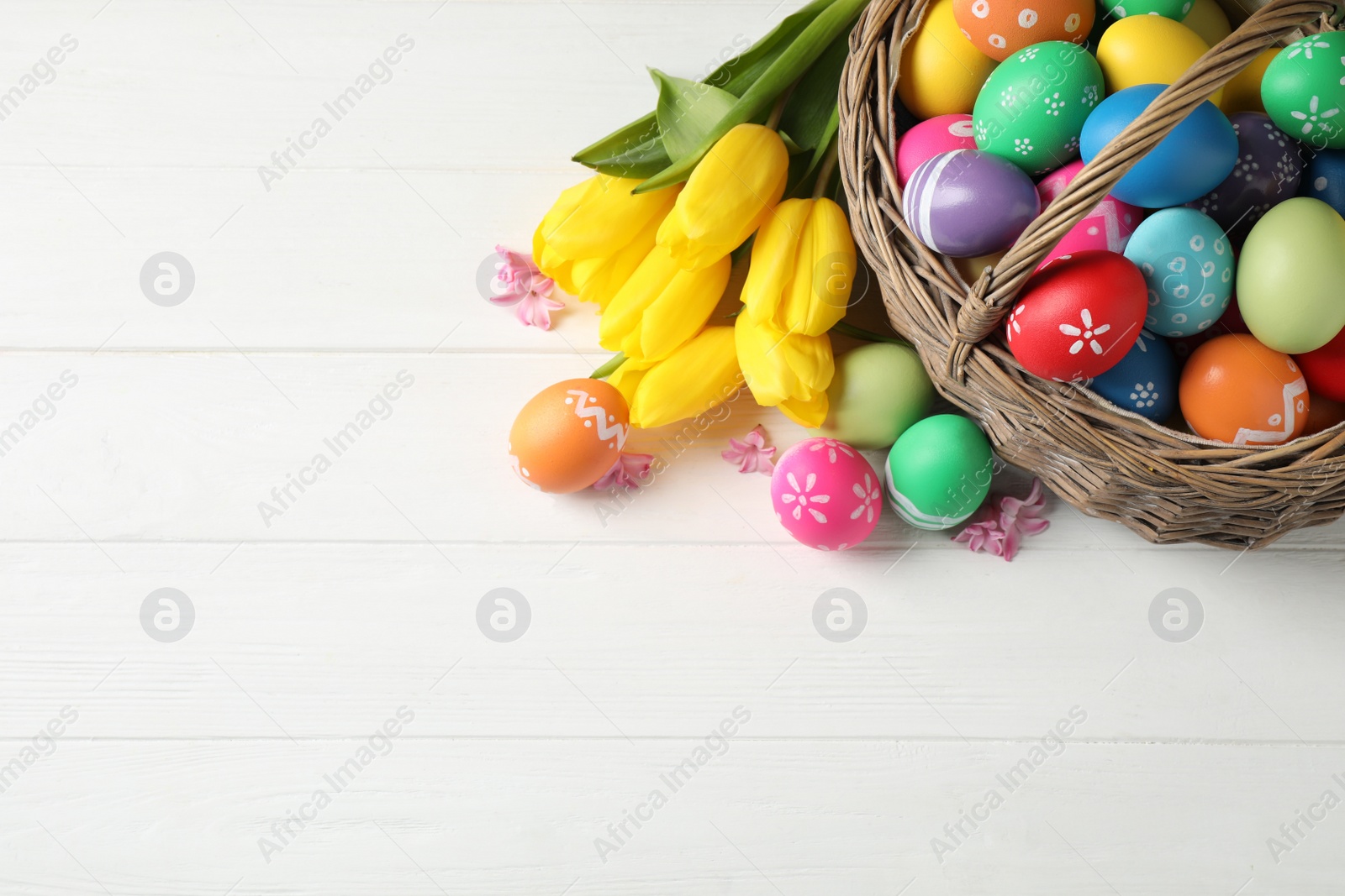 Photo of Colorful Easter eggs and flowers on white wooden background, flat lay. Space for text