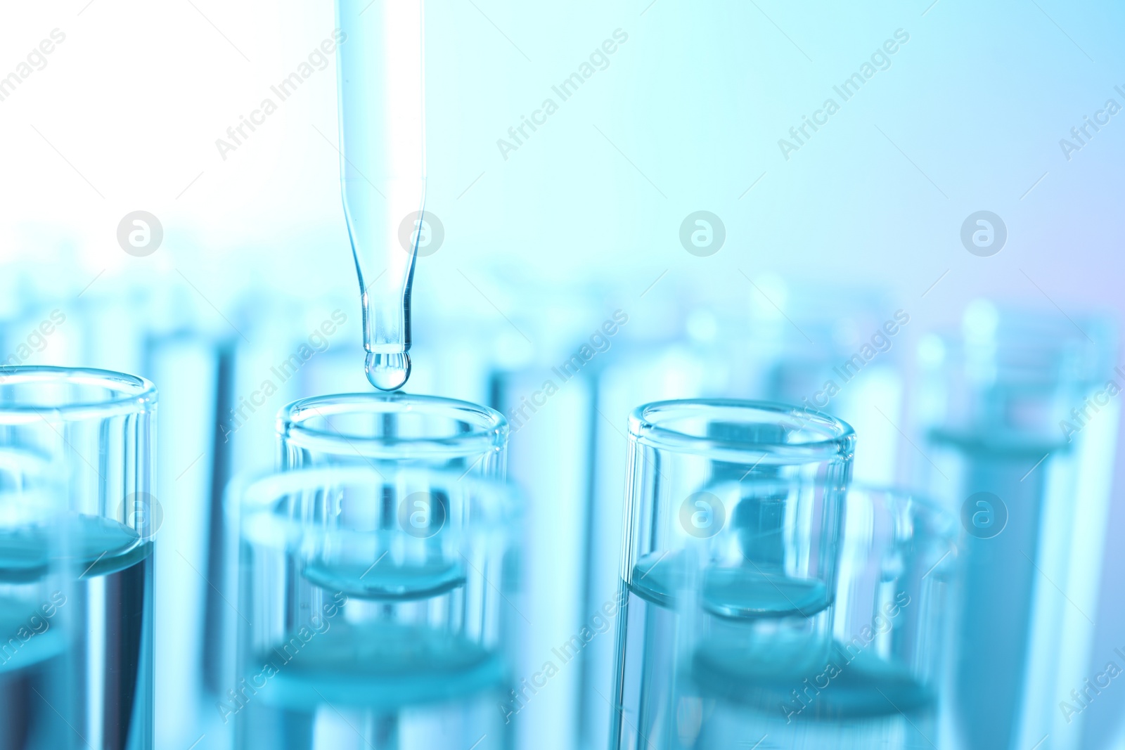 Photo of Dripping liquid from pipette into test tube on light blue background, closeup