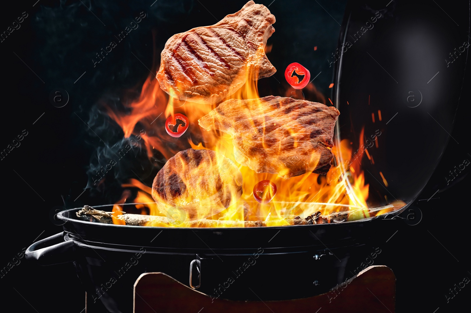 Image of Meat and chili pepper slices falling onto barbecue grill with flame against black background, closeup