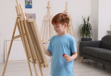 Little boy painting in studio. Using easel to hold canvas