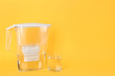Filter jug and glass with purified water on yellow background. Space for text