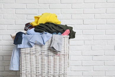 Laundry basket with dirty clothes near brick wall. Space for text