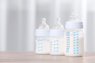 Photo of Feeding bottles with milk on wooden table indoors. Space for text