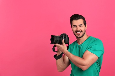 Photo of Young photographer with professional camera on pink background. Space for text