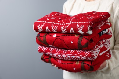 Photo of Woman holding stack of different Christmas sweaters on grey background, closeup. Space for text