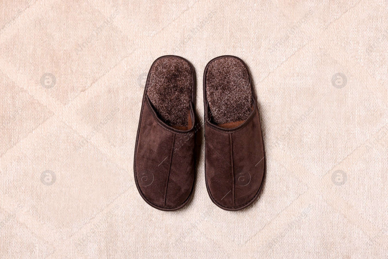 Photo of Brown slippers on soft carpet, top view