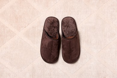 Brown slippers on soft carpet, top view
