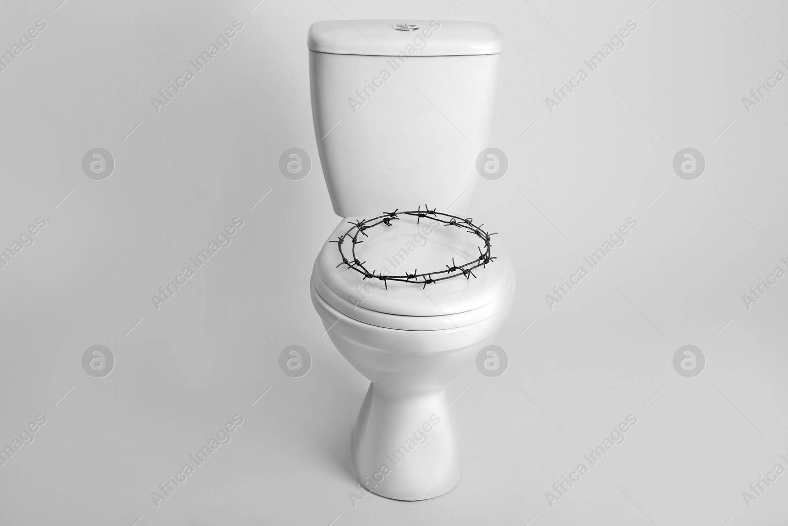 Photo of Toilet bowl with barbed wire on white background. Hemorrhoids concept