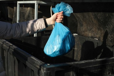 Woman throwing trash bag full of garbage in bin outdoors, closeup