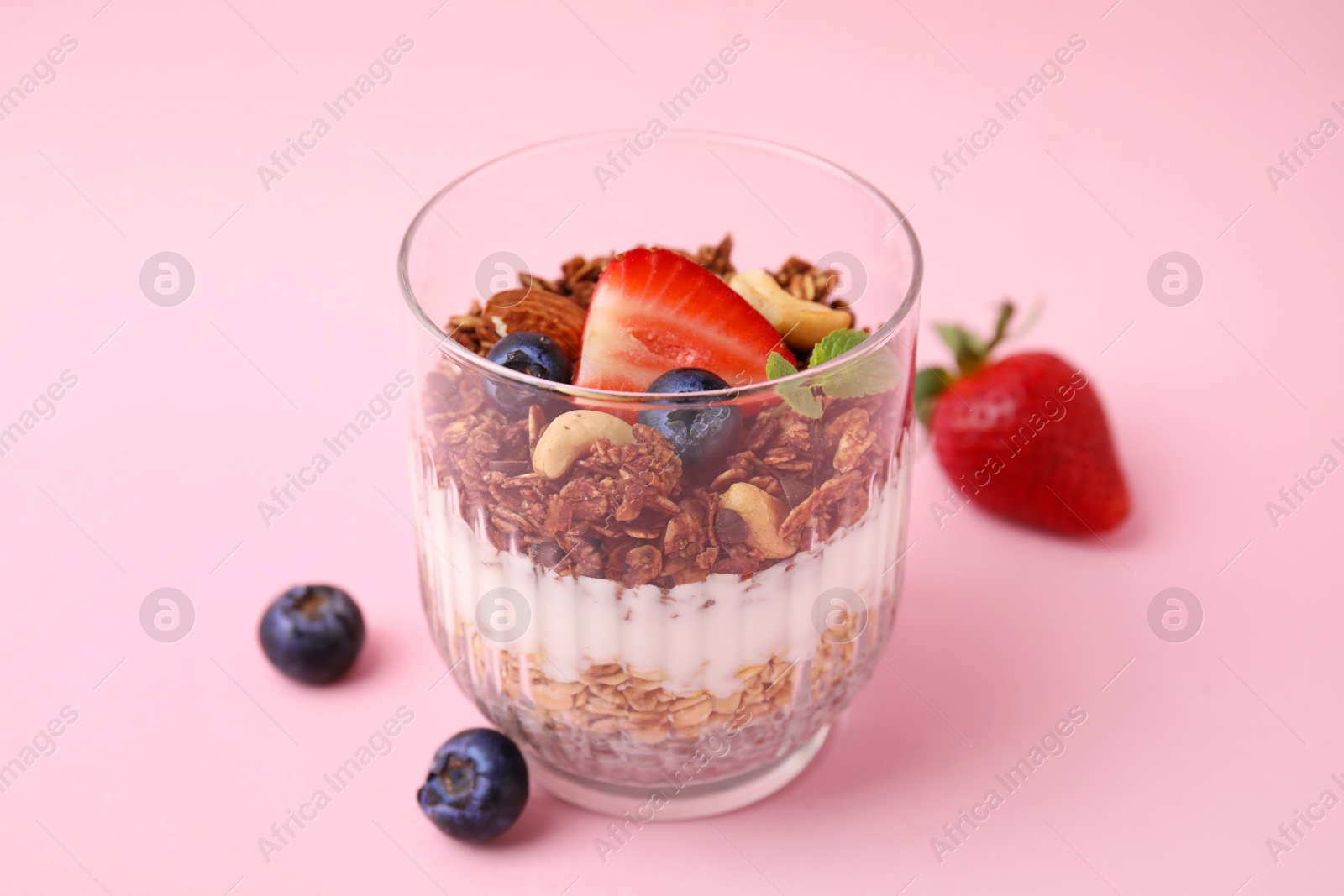 Photo of Tasty granola with berries, nuts, yogurt and chia seeds in glass on pink background, closeup