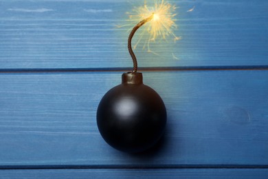 Image of Old fashioned black bomb with lit fuse on blue wooden table, top view