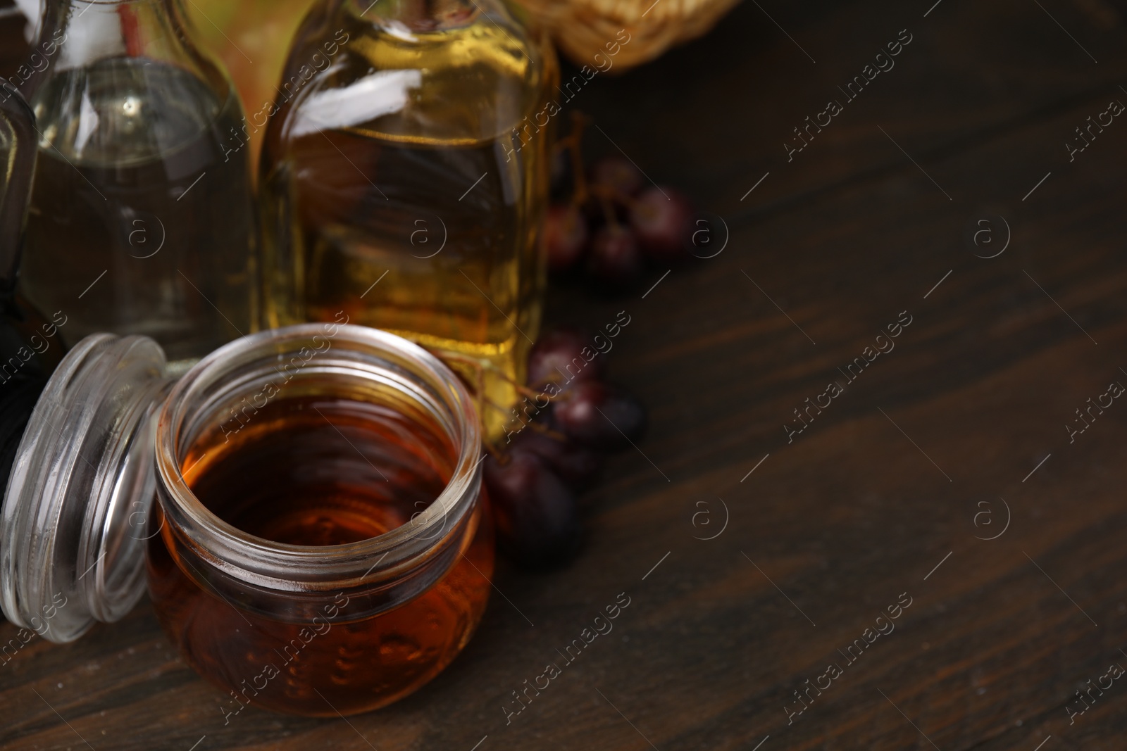 Photo of Different types of vinegar and grapes on wooden table, space for text