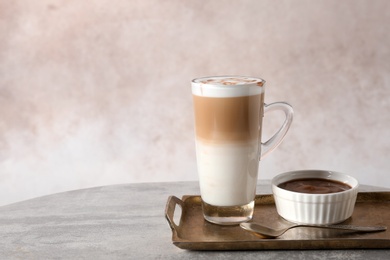 Tray with glass cup of caramel macchiato and syrup on table against color background. Space for text