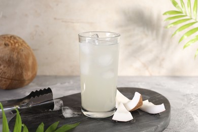 Photo of Glass of coconut water, ice cubes and nuts on grey table