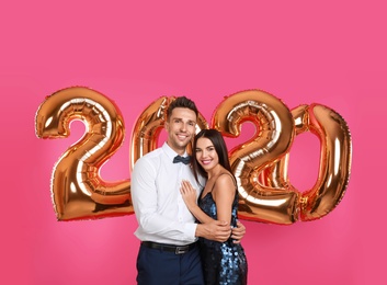 Happy young couple near golden 2020 balloons on pink background. New Year celebration