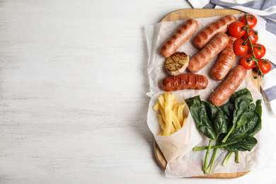 Tasty grilled sausages served on white wooden table, flat lay. Space for text