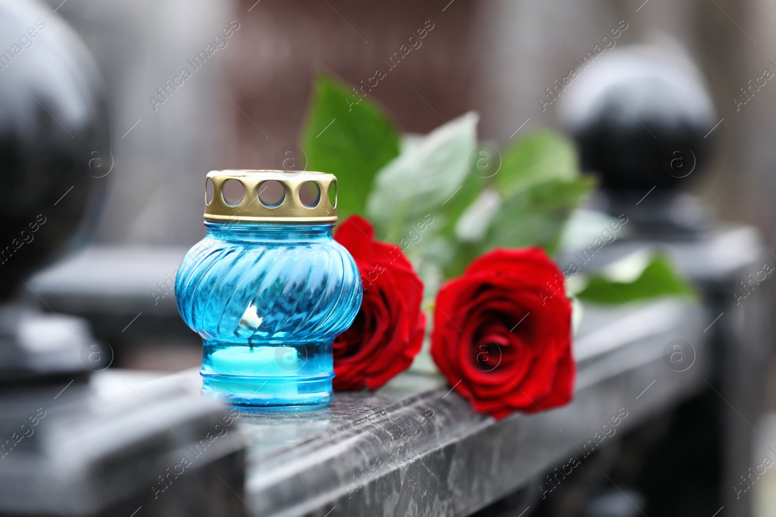 Photo of Red roses and candle on black marble tombstone outdoors. Funeral ceremony