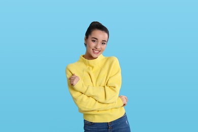 Photo of Beautiful young woman wearing yellow warm sweater on light blue background