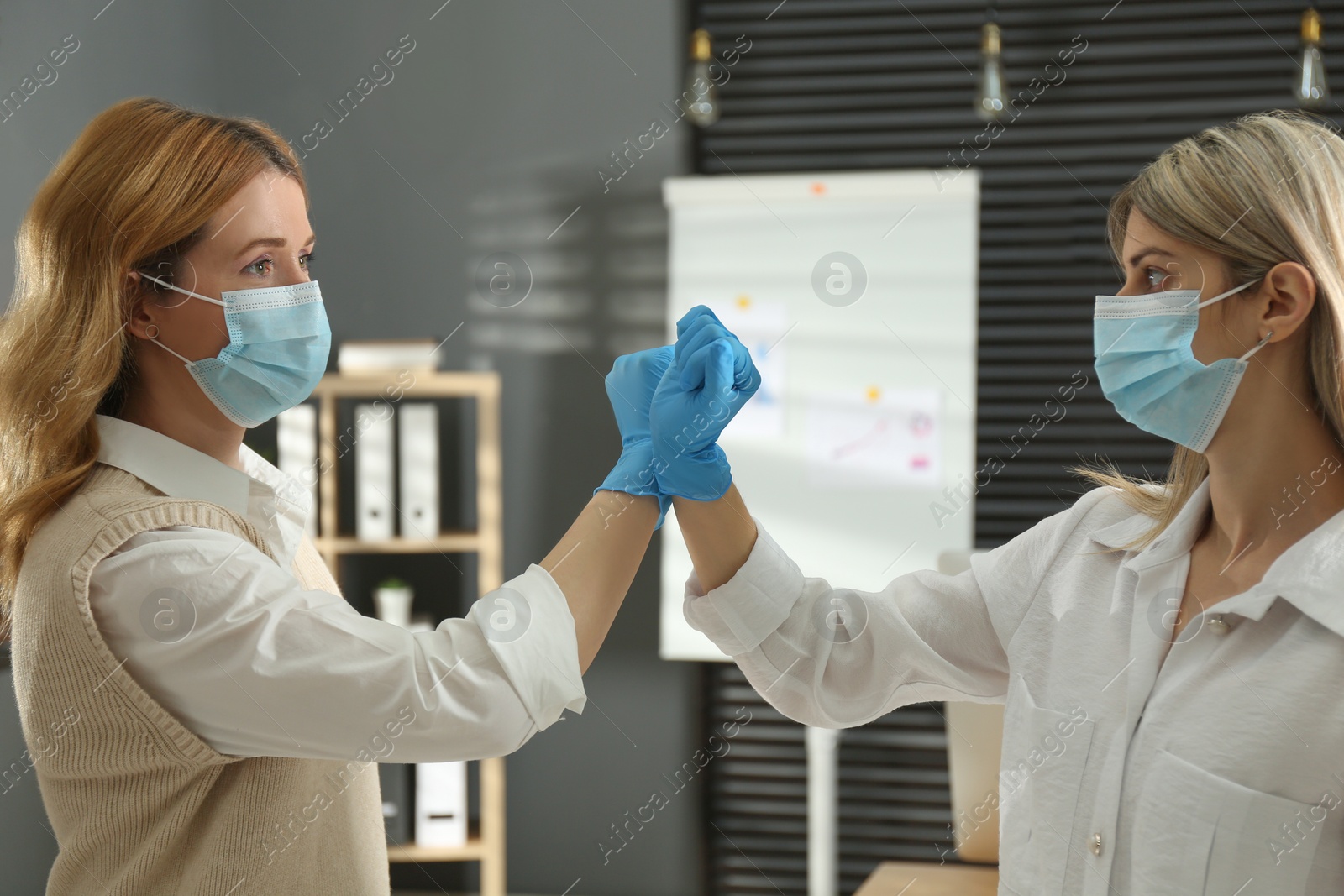 Photo of People greeting each other by bumping fists instead of handshake indoors