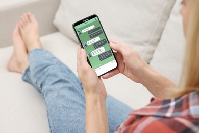 Woman texting via mobile phone indoors, closeup. Device screen with messages