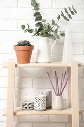 Photo of Beautiful plants and accessories on shelves near brick wall at home