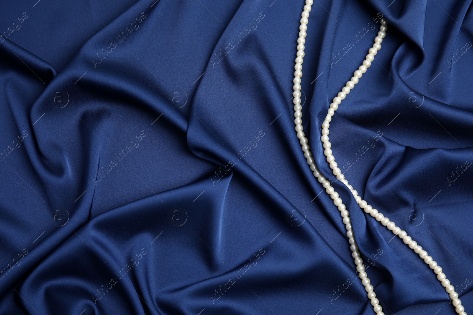 Photo of Beautiful pearls on dark blue silk, top view. Space for text