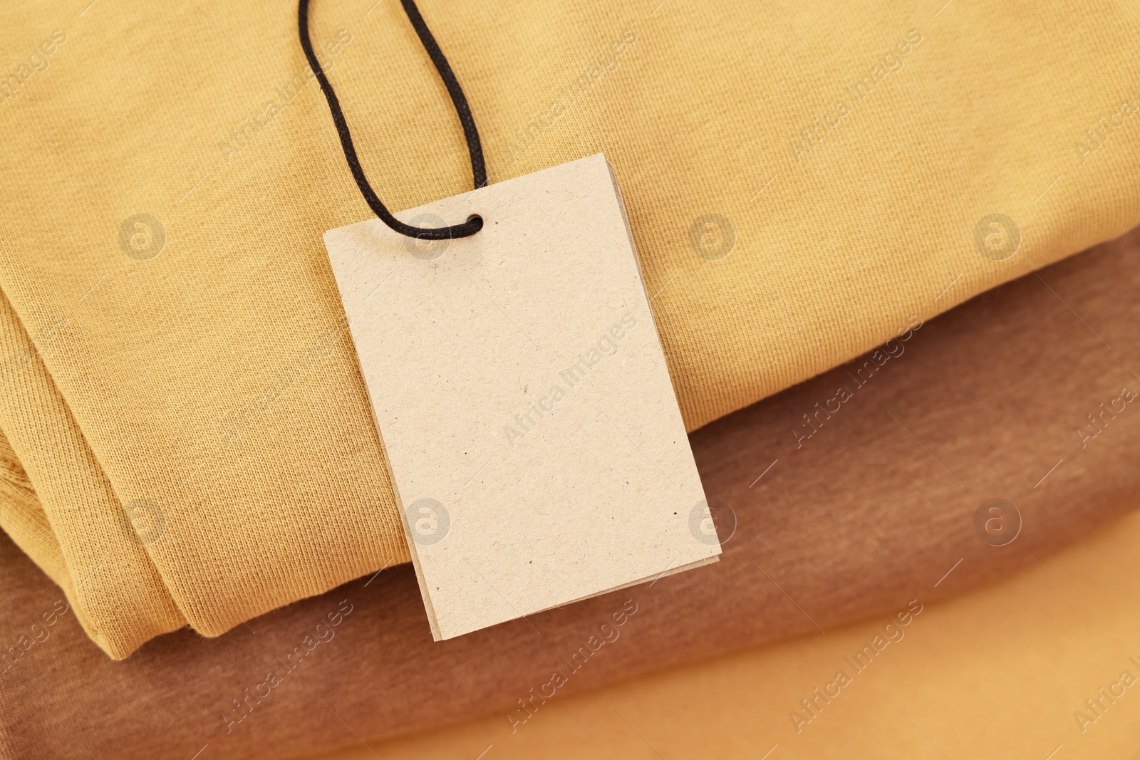 Photo of Garment with cardboard tag on beige background, closeup. Space for text