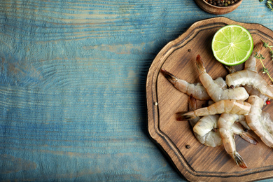 Photo of Fresh raw shrimps and cut lime on blue wooden table, top view. Space for text