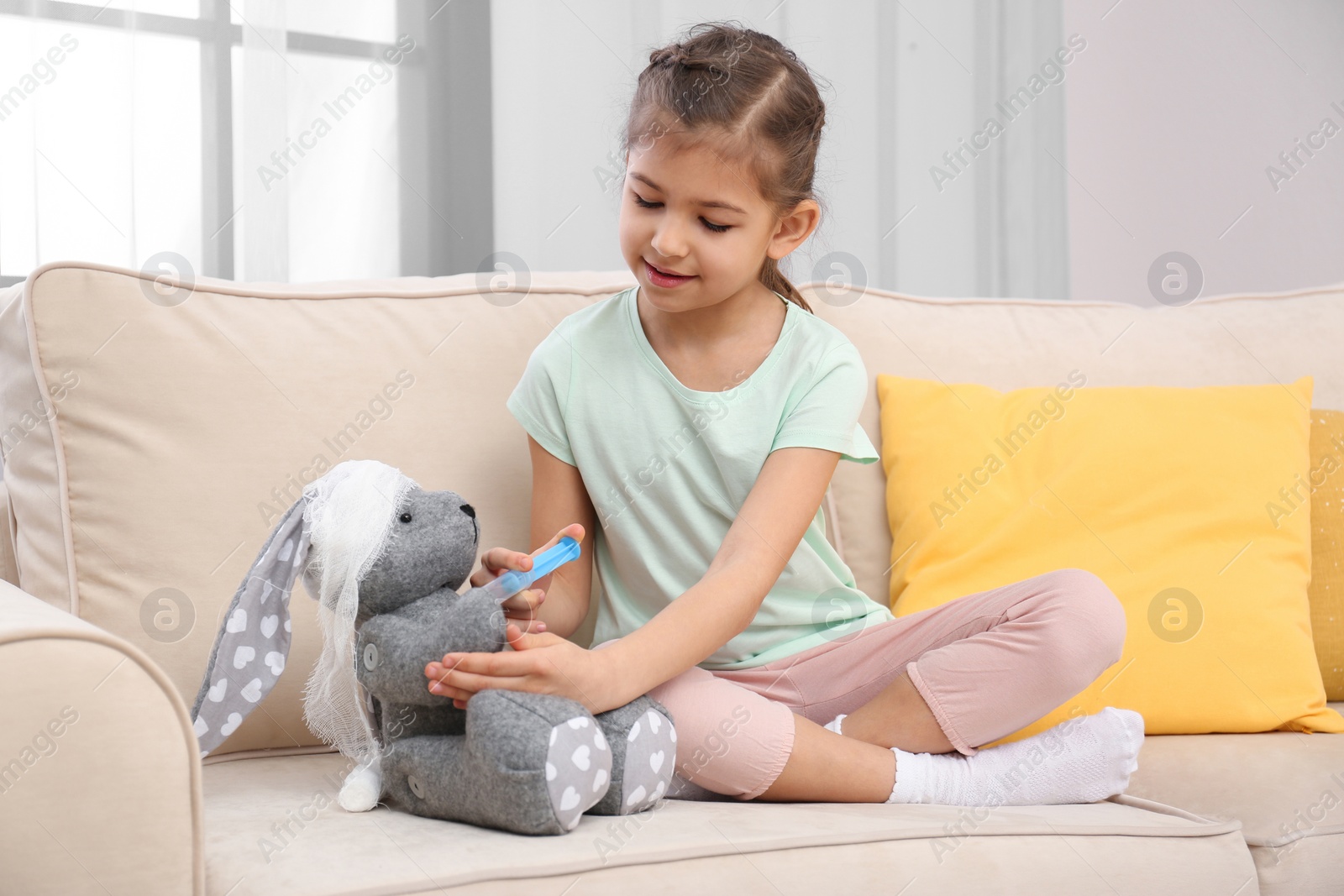 Photo of Cute child playing doctor with stuffed toy on sofa in hospital