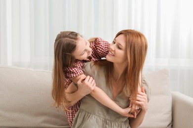 Mother with her cute daughter spending time together on sofa at home