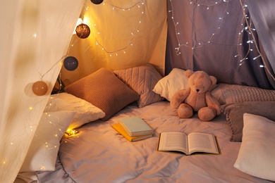 Photo of Play tent with books, pillows and Teddy bear. Modern children's room interior