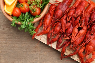 Photo of Delicious red boiled crayfish and products in bowl on wooden table, top view
