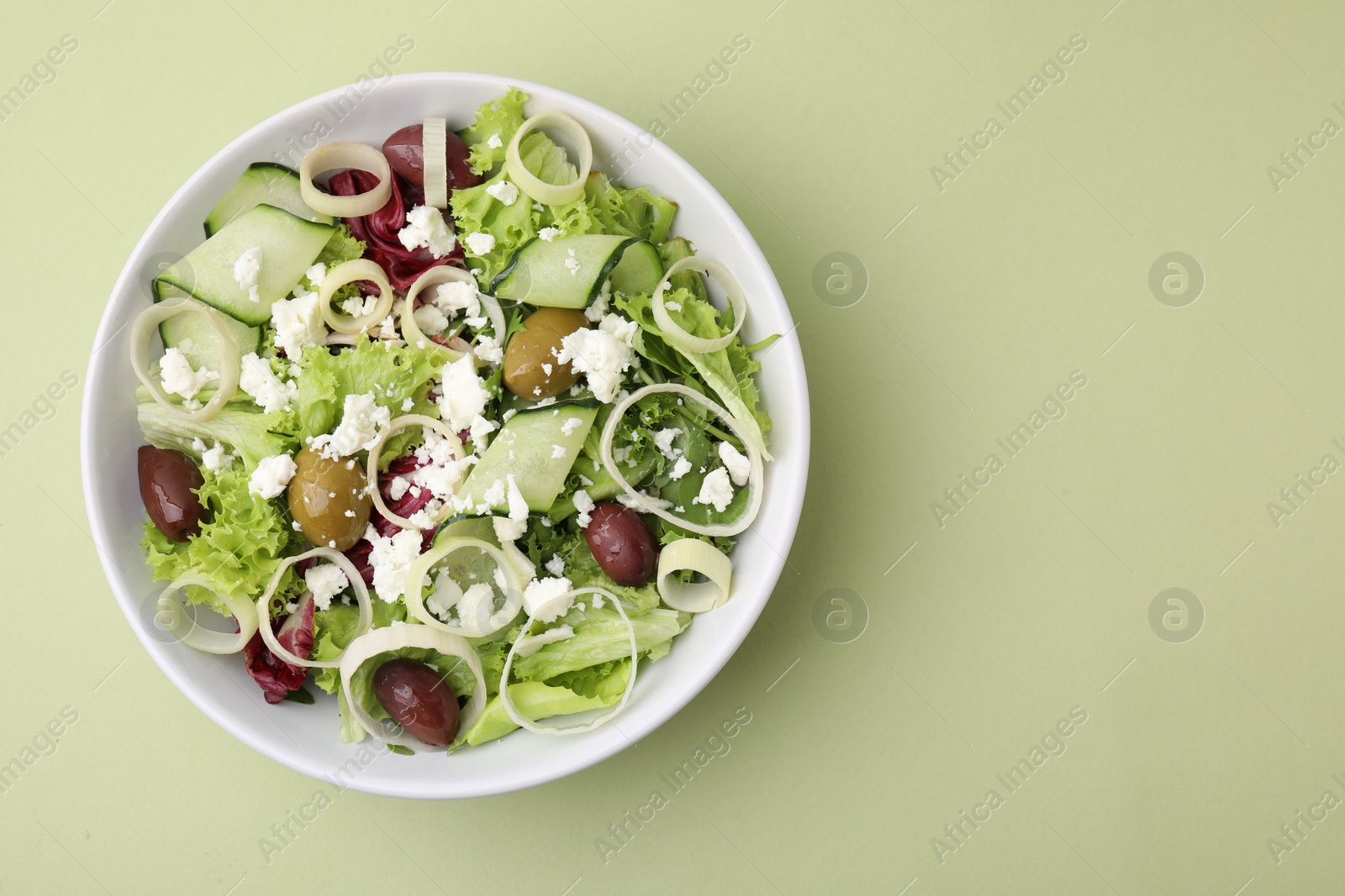 Photo of Bowl of tasty salad with leek, olives and cheese on pale green table, top view. Space for text